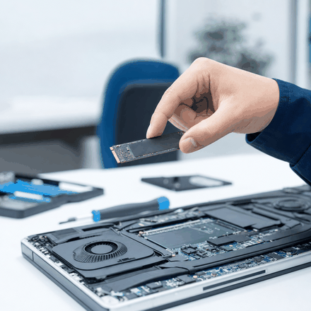 SSDを手に持つ手元と、開けたノートPC